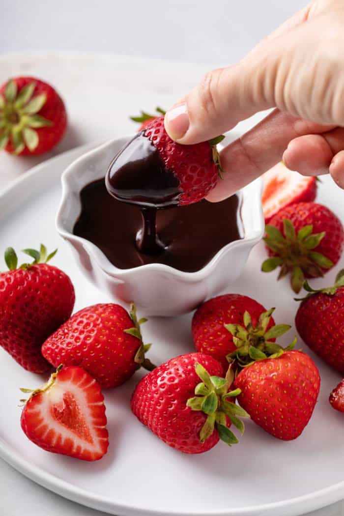 Strawberry being dipped into a white bowl of hot fudge sauce.