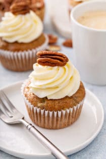 Frosted hummingbird cupcake next to a fork on a white plate