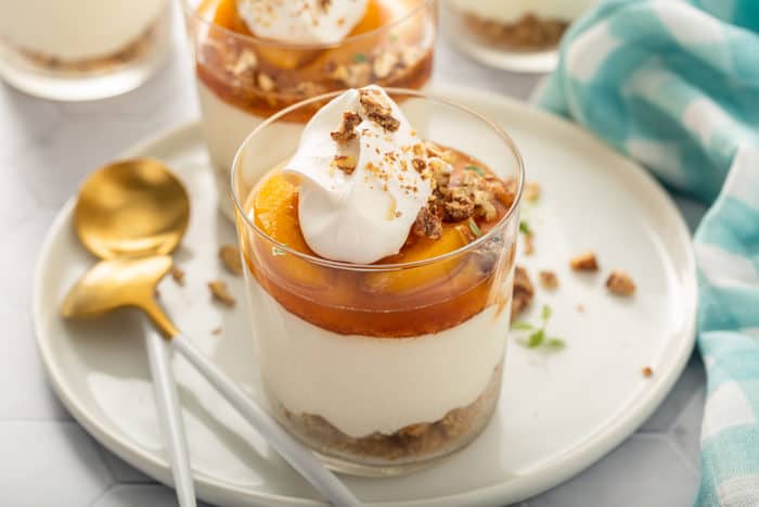 Layered no-bake peach cheesecake on a white plate next to a spoon