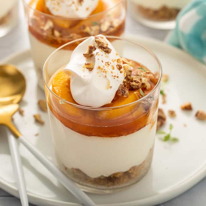 Layered no-bake peach cheesecake on a white plate next to a spoon