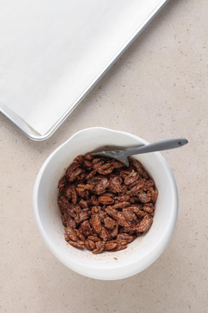 Pecans coated with cinnamon-sugar coating in a white bowl.