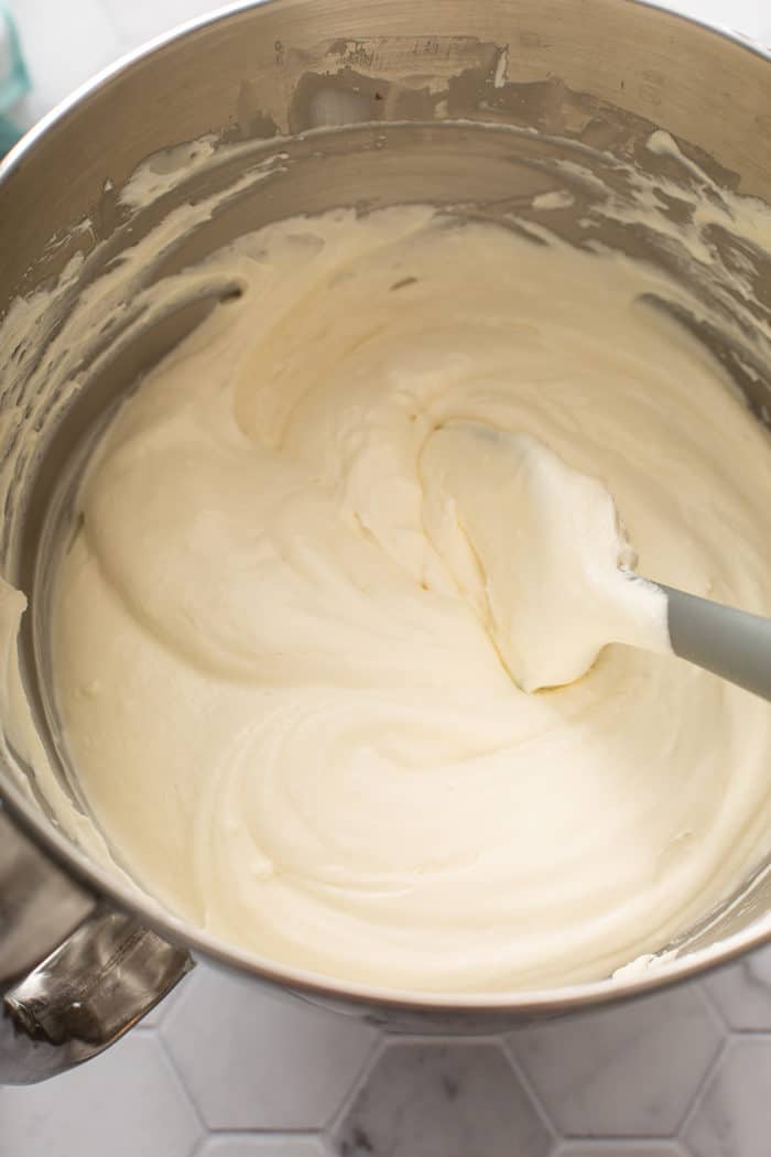 Spatula stirring together no bake peach cheesecake filling in a metal bowl