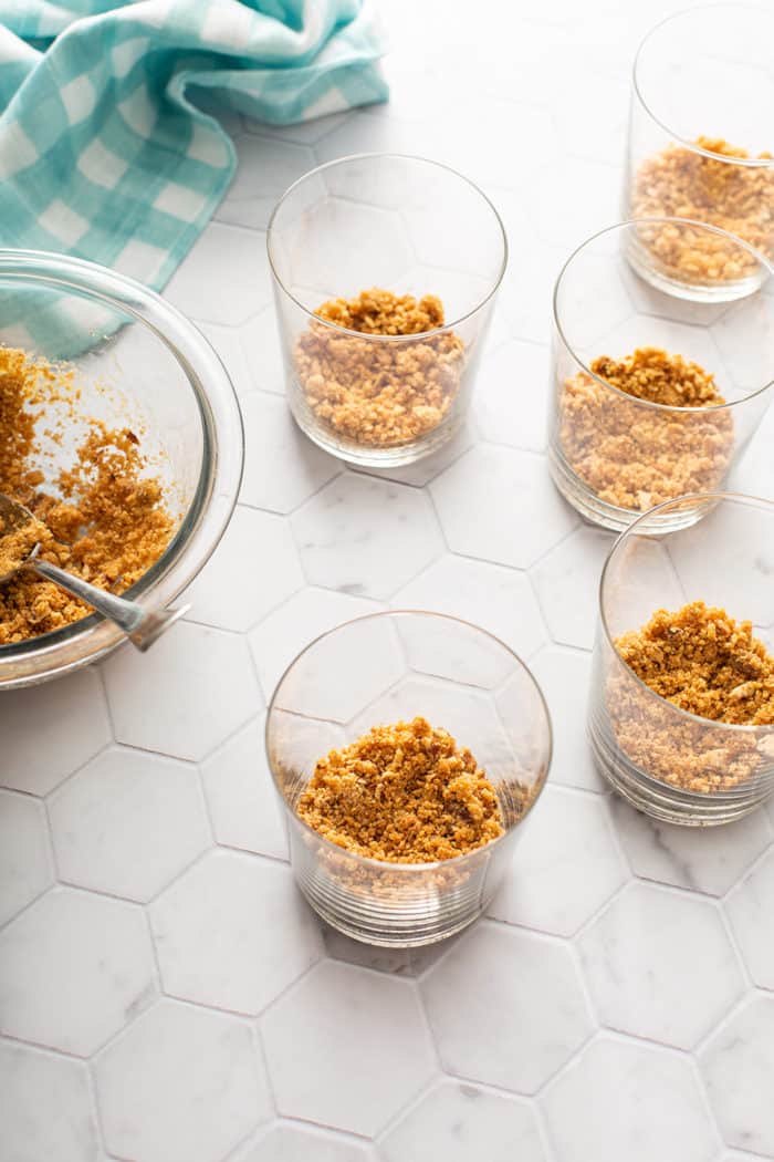 Crust for no-bake peach cheesecakes being added to the bottom of individual serving dishes