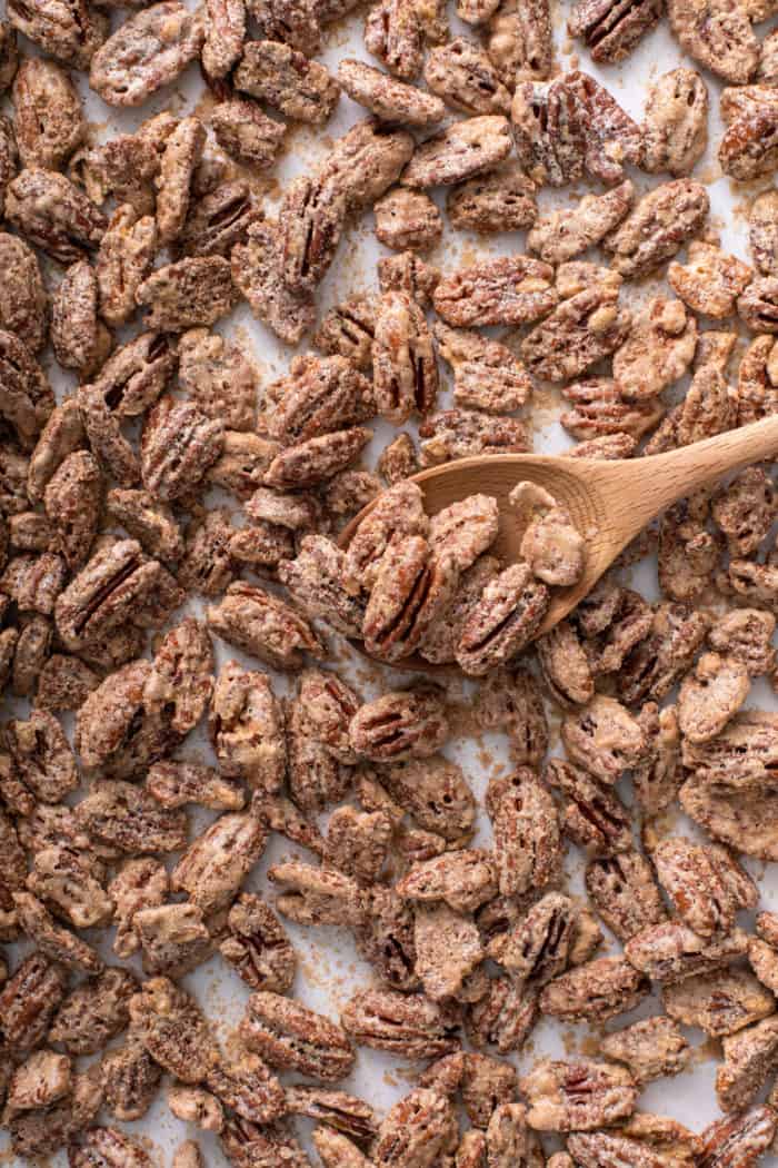 Wooden spoon stirring candied pecans on a parchment-lined baking sheet.