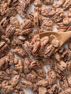 Candied pecans on a baking sheet being stirred with a wooden spoon.