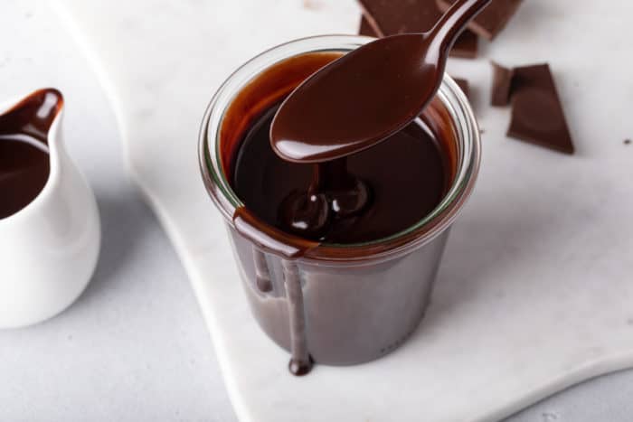 Spoon holding hot fudge sauce being held over a jar of the sauce.