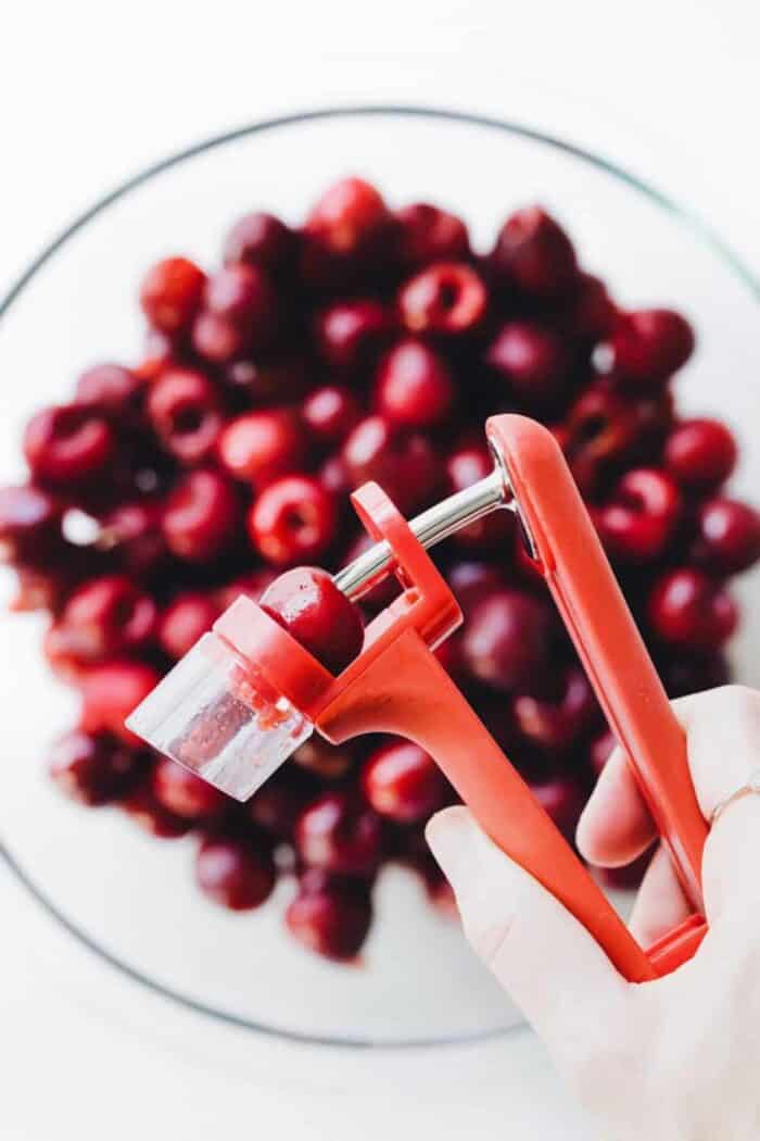 Close up of a cherry in a cherry pitter over a bowl of cherries