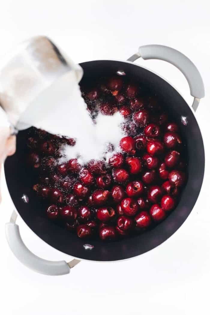 Sugar being poured over a pot of cherries for cherry pie filling