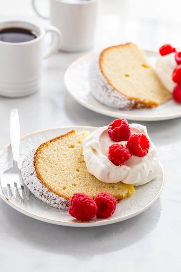 Two white plates with slices of cream cheese pound cake garnished with whipped cream and fresh berries