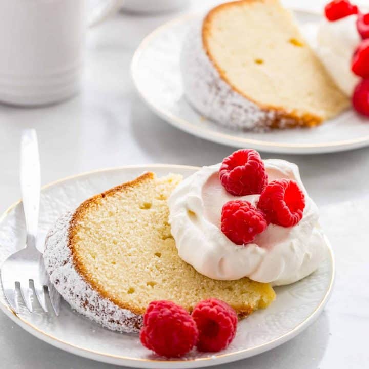 Two white plates with slices of cream cheese pound cake garnished with whipped cream and fresh berries
