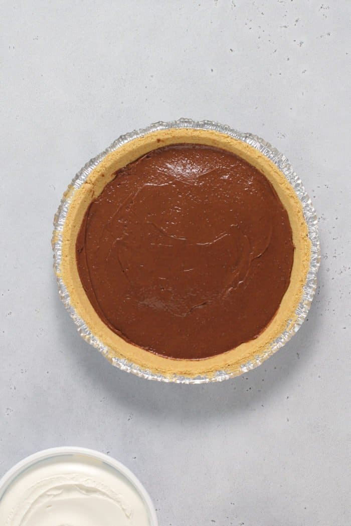 Graham cracker crust filled with chocolate pudding filling on a gray countertop.