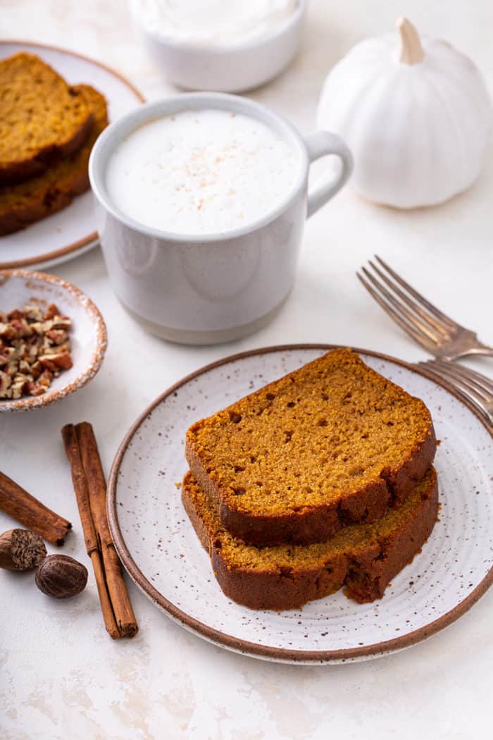 Two slices of pumpkin bread on a plate next to a cup of coffee