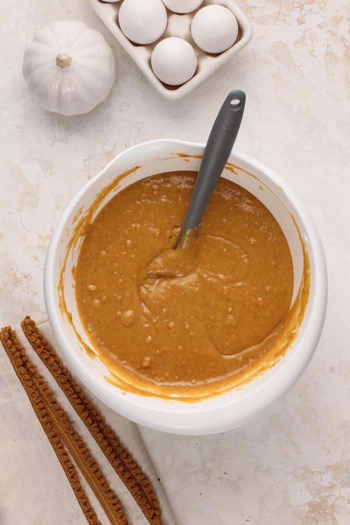 Spatula stirring together pumpkin bread batter in a white mixing bowl