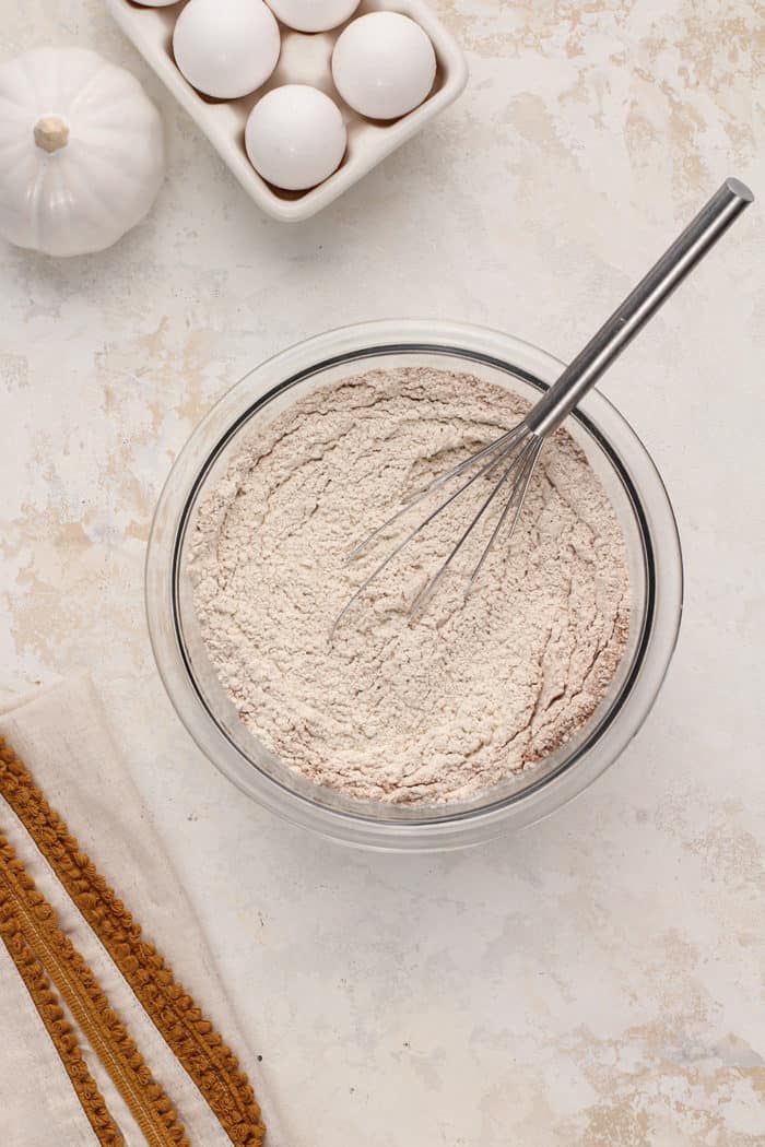 Whisk stirring together the dry ingredients for pumpkin bread in a glass mixing bowl