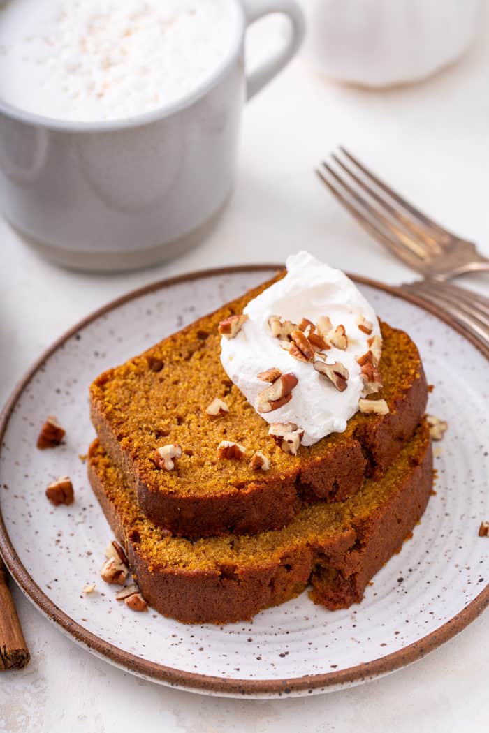 Two slices of pumpkin bread topped with whipped cream on a plate