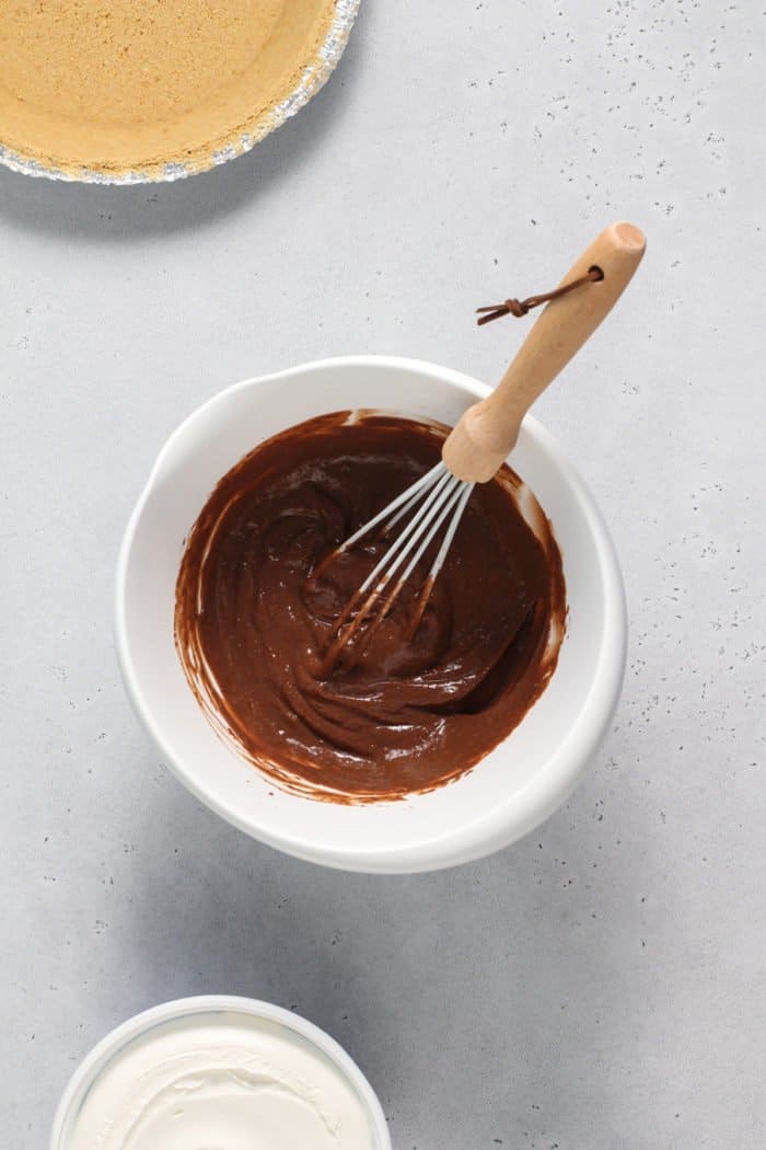 Chocolate filling for s'mores pie being whisked together in a white bowl.