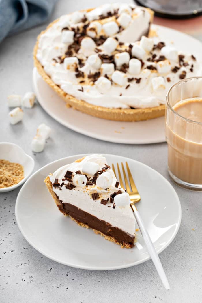 White plate with a slice of s'mores pie set in front of the full pie in the background.