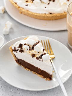 Slice of s'mores pie next to a white and gold fork on a white plate.
