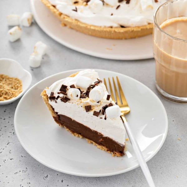 Slice of s'mores pie next to a white and gold fork on a white plate.