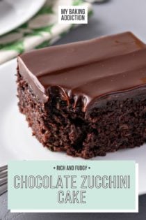 Slice of chocolate zucchini cake set on a white plate. A bite has been taken from the corner of the cake. Text overly includes recipe name.