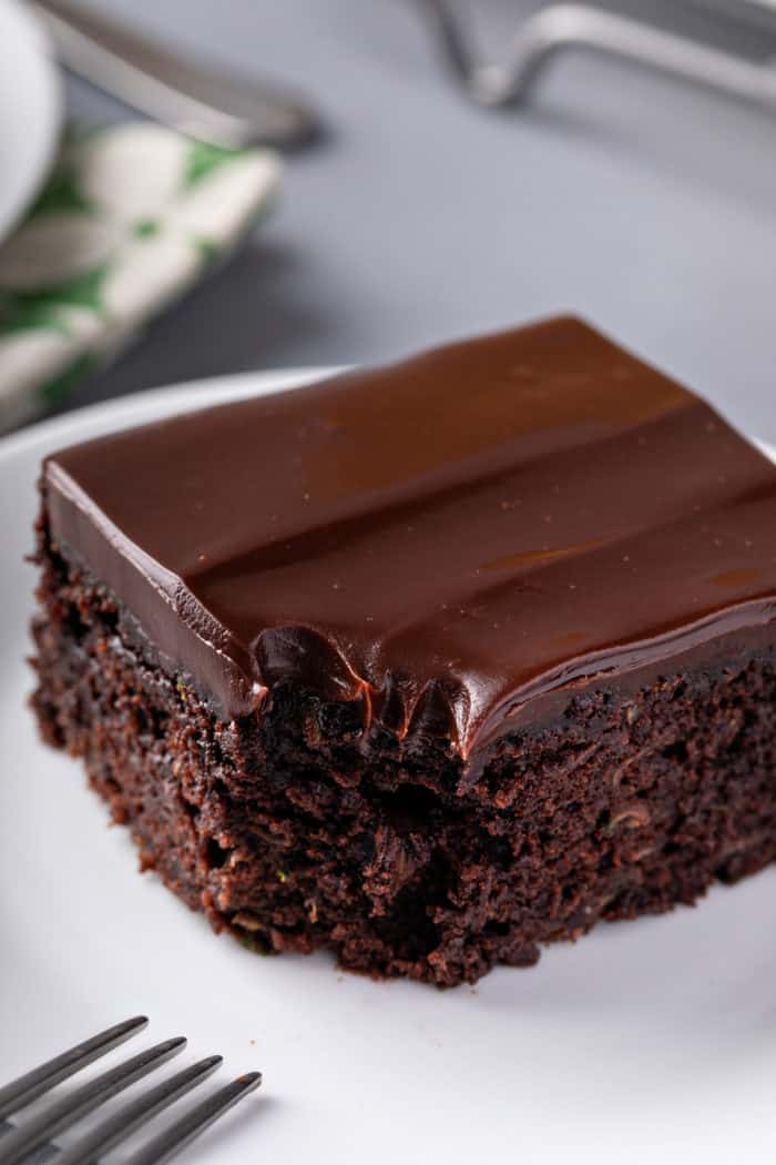 Close up of a slice of chocolate zucchini cake with a bite taken from the corner. A fork is visible perched on the side of the plate.