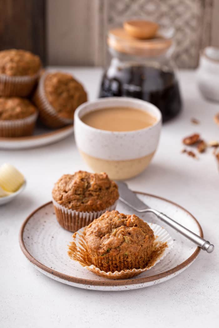 Two morning glory muffins on a plate with a mug of coffee in the background.