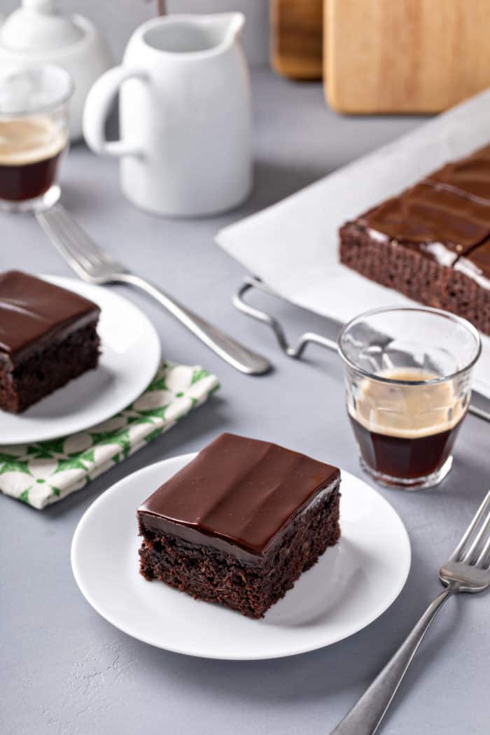 Two plates of chocolate zucchini cake next to cups of espresso.