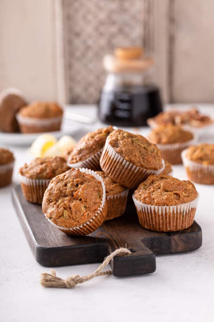 Morning glory muffins piled on a wooden board. A pot of coffee is visible in the background.