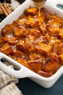 Baked bread pudding topped with caramel sauce in a white baking dish