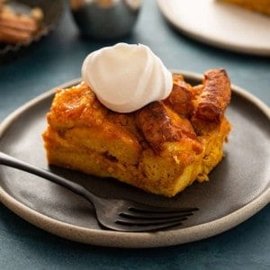 Slice of pumpkin bread pudding topped with whipped cream next to a fork on a plate