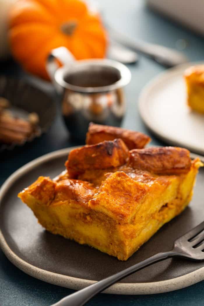 Slice of pumpkin bread pudding next to a fork on a dark plate