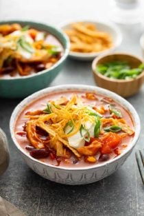 Close up of chicken chili topped with sour cream and cheese in a white bowl