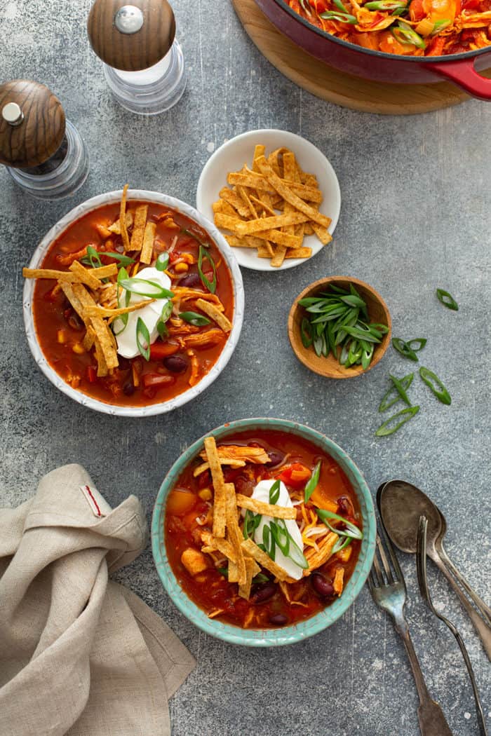 Overhead view of two bowls of easy chicken chili surrounded by bowls of toppings