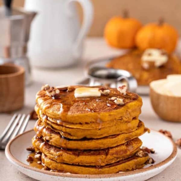 White plate with a stack of pumpkin pancakes topped with butter and maple syrup.