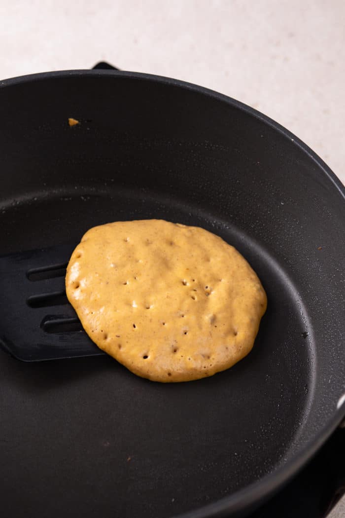 Spatula about to flip a pumpkin pancake in a cast iron skillet.