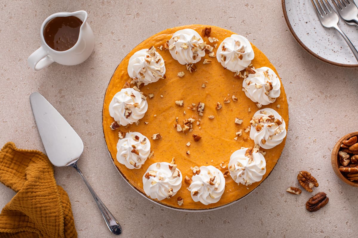 Overhead view of sweet potato cheesecake topped with dollops of whipped cream and chopped pecans.
