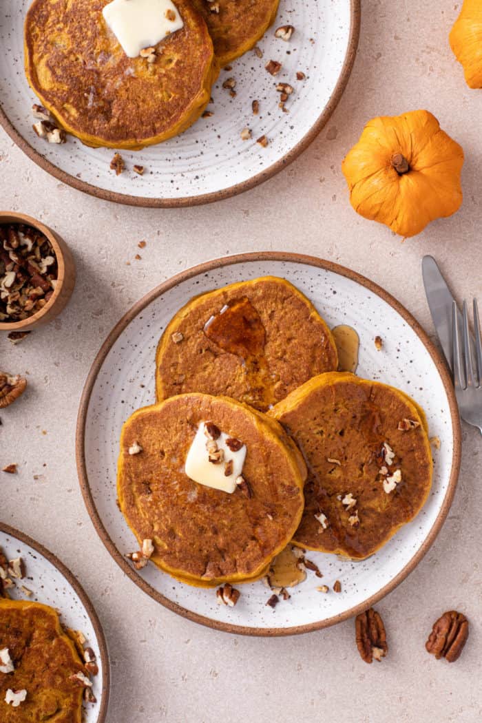 Overhead view of three plates of pumpkin pancakes, topped with butter and syrup.