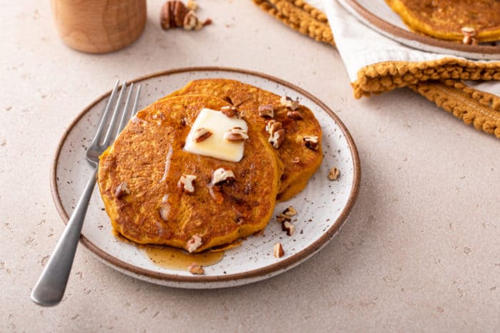 Two pumpkin pancakes next to a fork on a speckled plate.