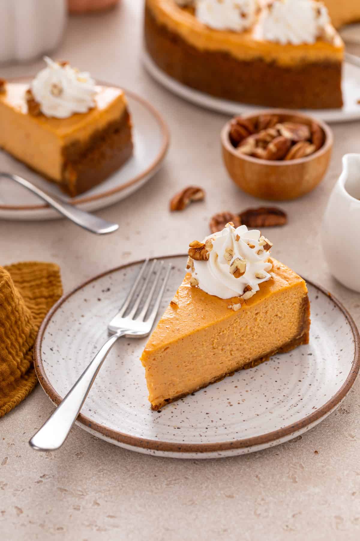 Slice of sweet potato cheesecake next to a fork on a stoneware plate, with a second plated slice visible in the background.