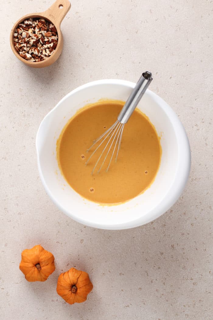 Wet ingredients for pumpkin pancakes being whisked in a white mixing bowl.