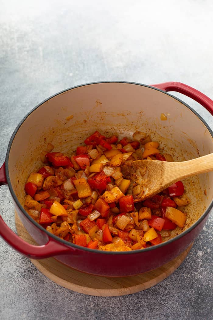 Wooden spoon stirring sauteed peppers with spices in a dutch oven