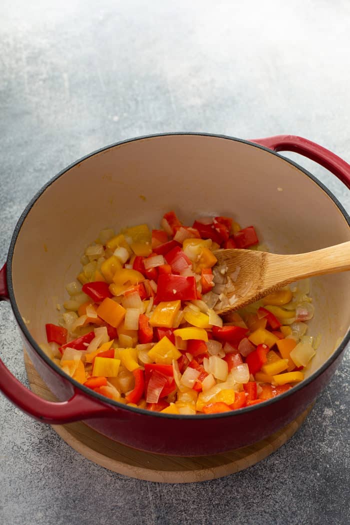 Sauteed onions and peppers being stirred in a dutch oven