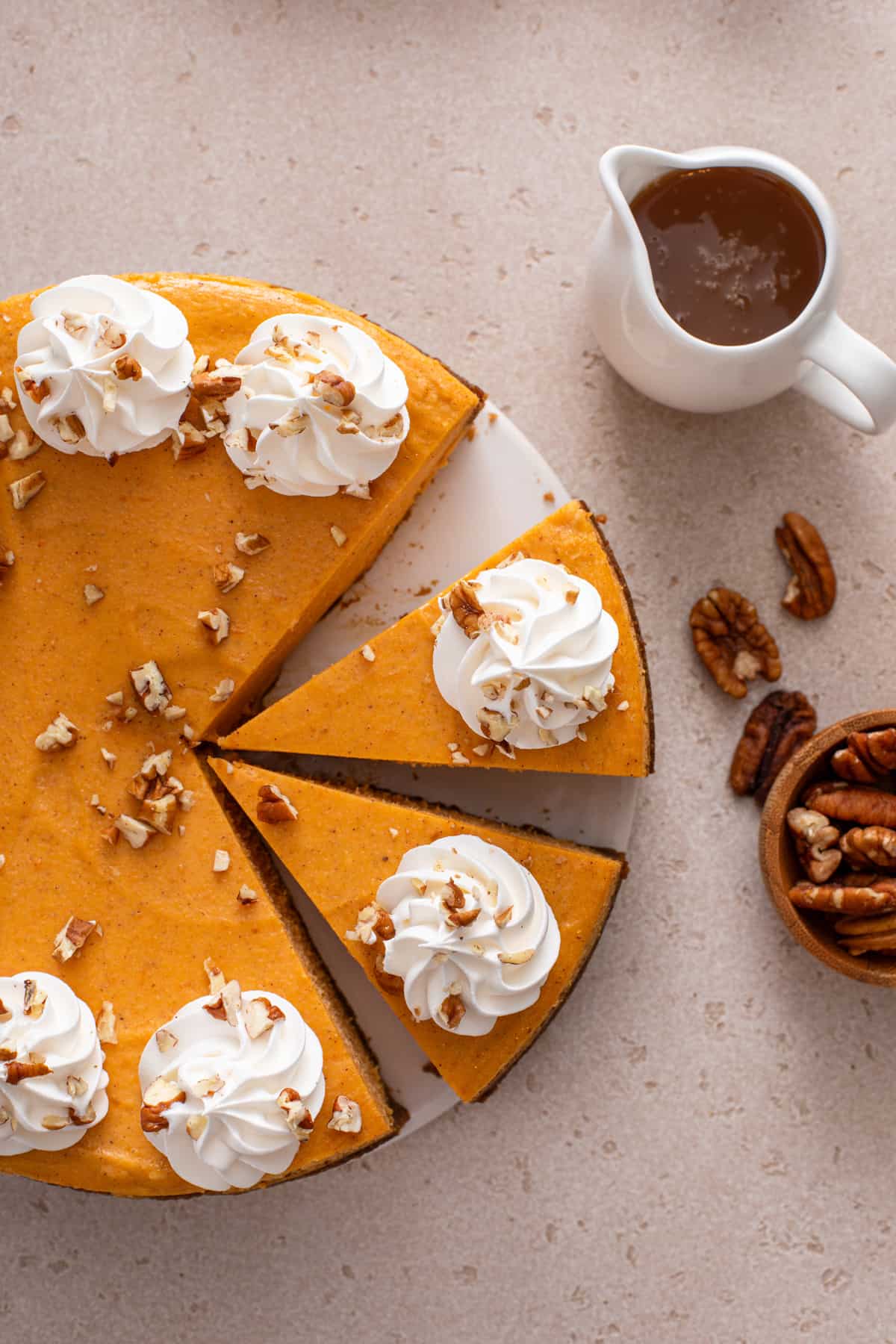 Overhead view of sliced sweet potato cheesecake, topped with dollops of whipped cream and chopped pecans.