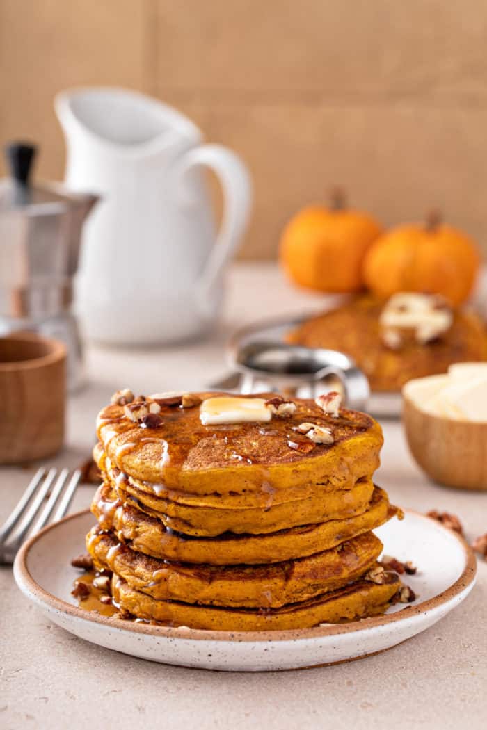White plate with a stack of pumpkin pancakes topped with butter and maple syrup.