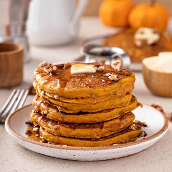 Stack of pumpkin pancakes topped with butter and syrup.