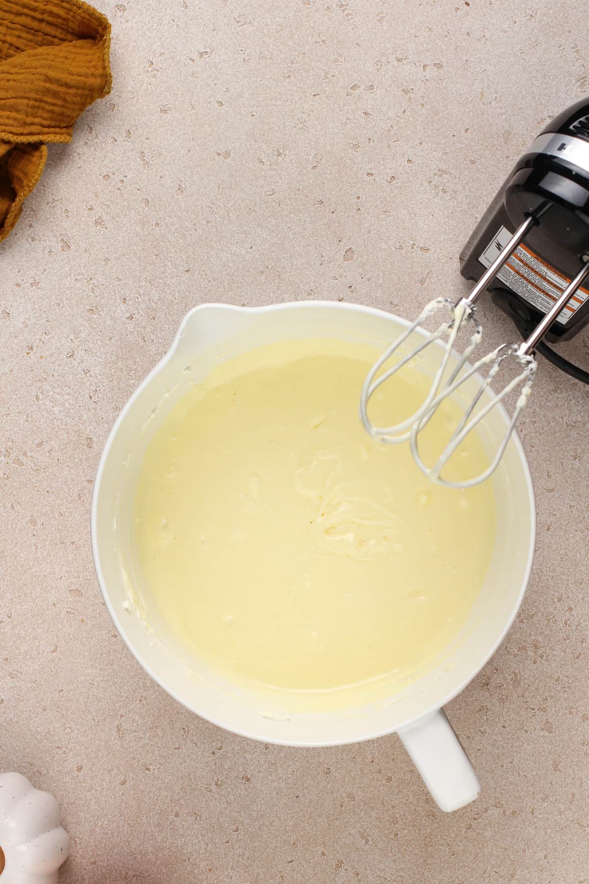 Eggs added to cream cheese and sugar in a white mixing bowl.