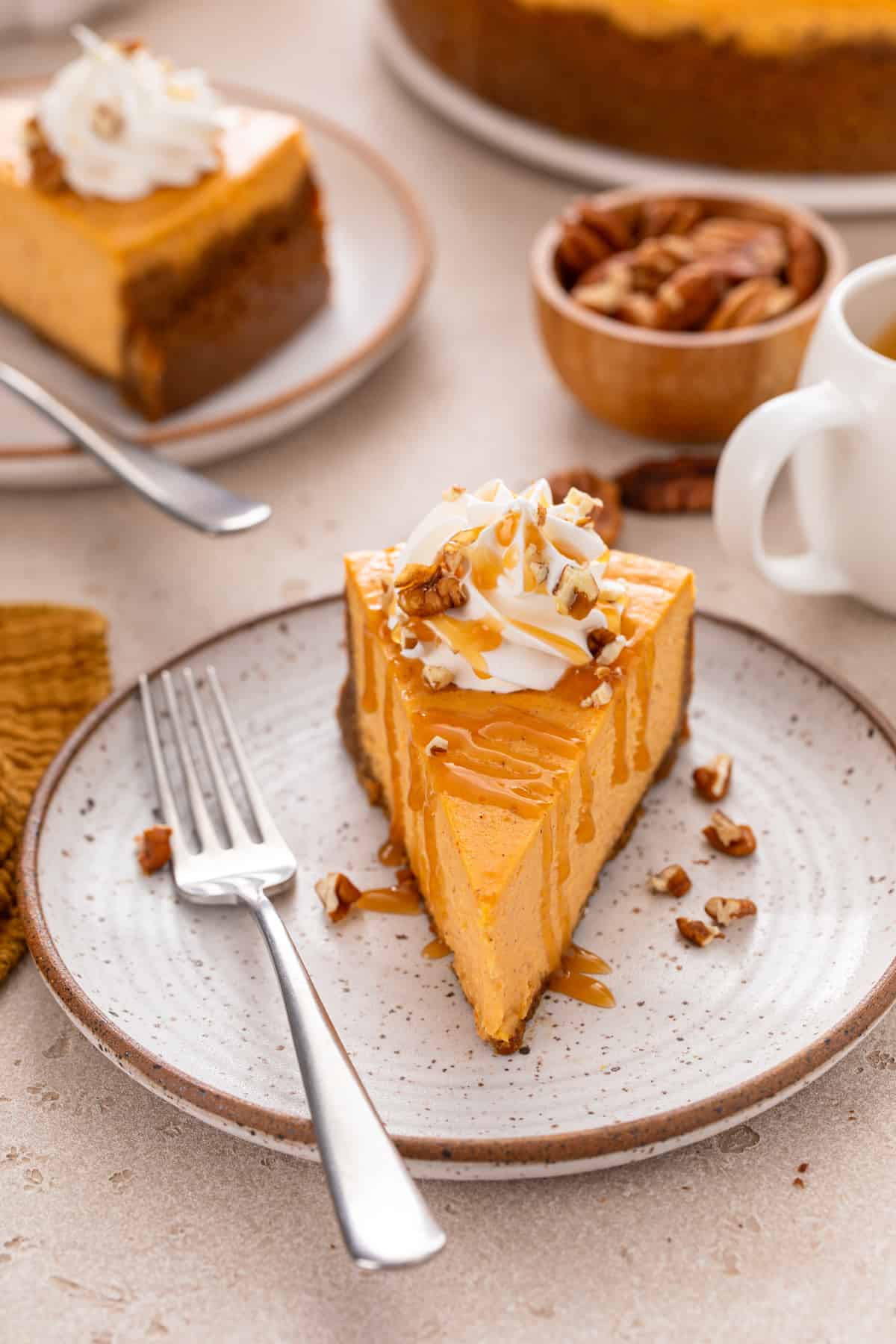 Slice of sweet potato cheesecake topped with salted caramel sauce, whipped cream, and chopped pecans.
