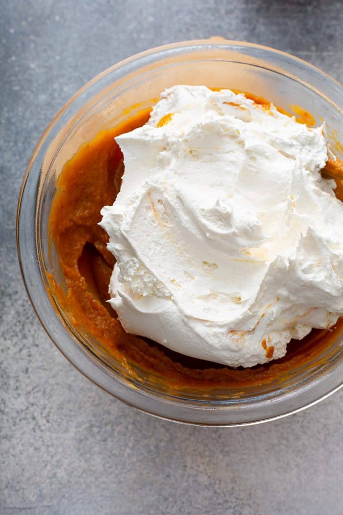 Whipped topping being added to pumpkin pie filling in a glass mixing bowl