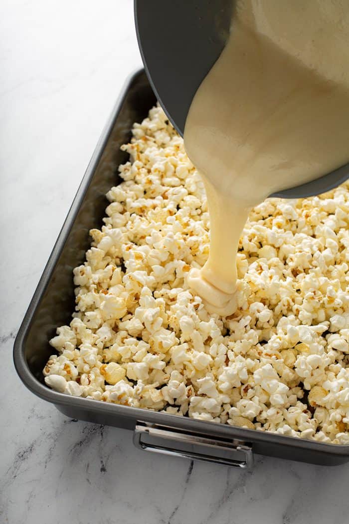 Light caramel being poured over a pan of popped popcorn