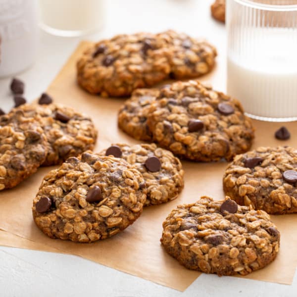 Banana Oatmeal cookies scattered on a piece of parchment paper next to a glass of milk.